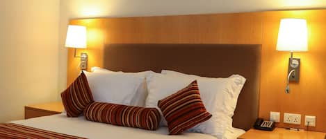 A hotel room with a large bed, two bedside tables, a wooden headboard, and two wall-mounted lamps.