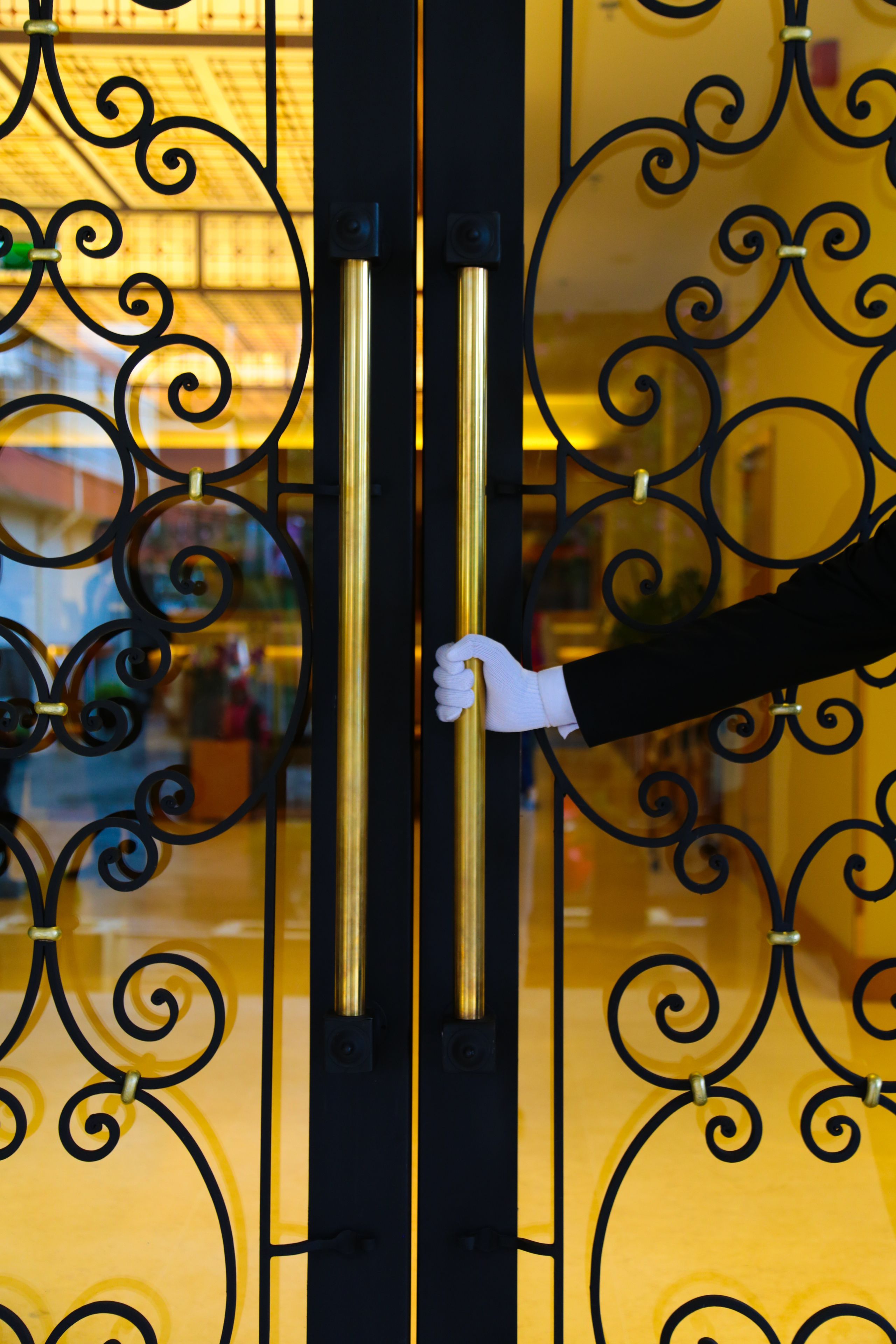 A hand on a golden door handle, with intricate black metalwork.