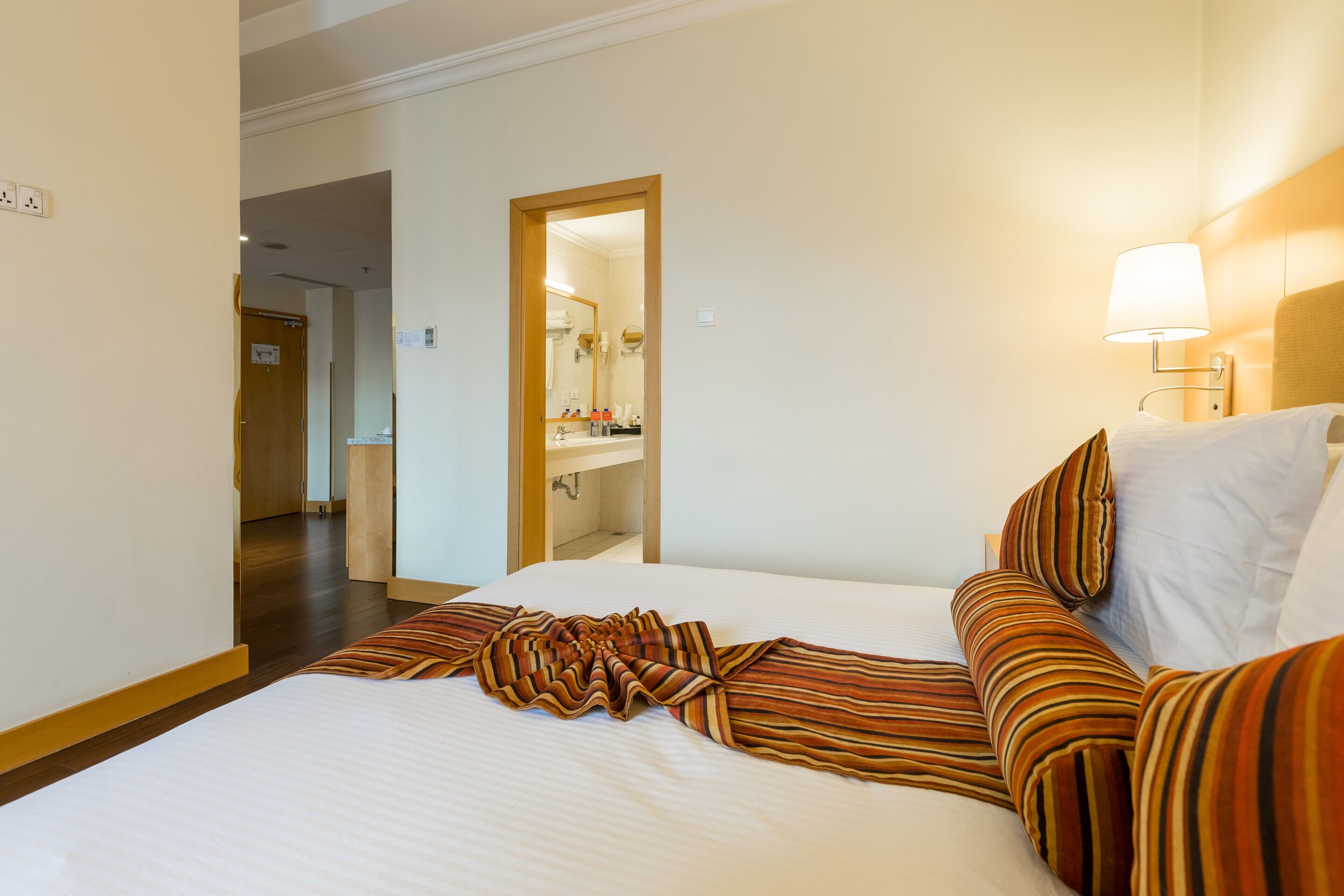 A hotel room with a large bed, a bedside lamp, and a view of the bathroom through an open door.