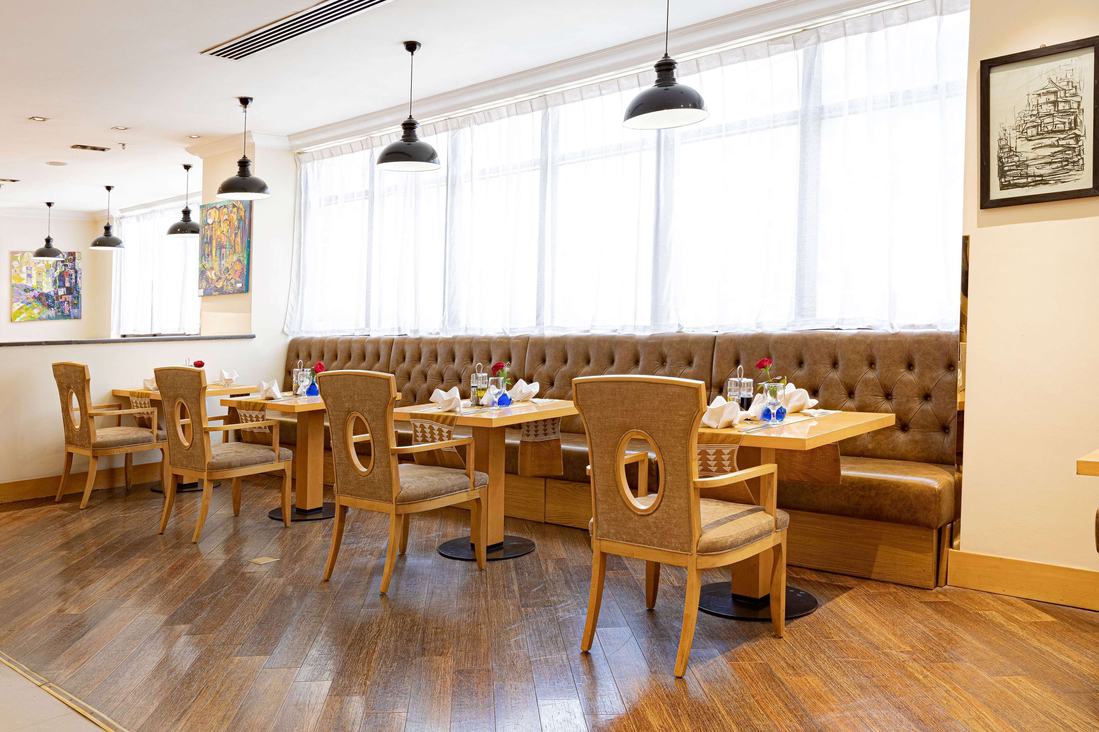 A dining area with wooden tables and chairs, a cushioned bench, and pendant lighting.