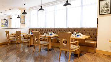 A dining area with wooden tables and chairs, a cushioned bench, and pendant lighting.