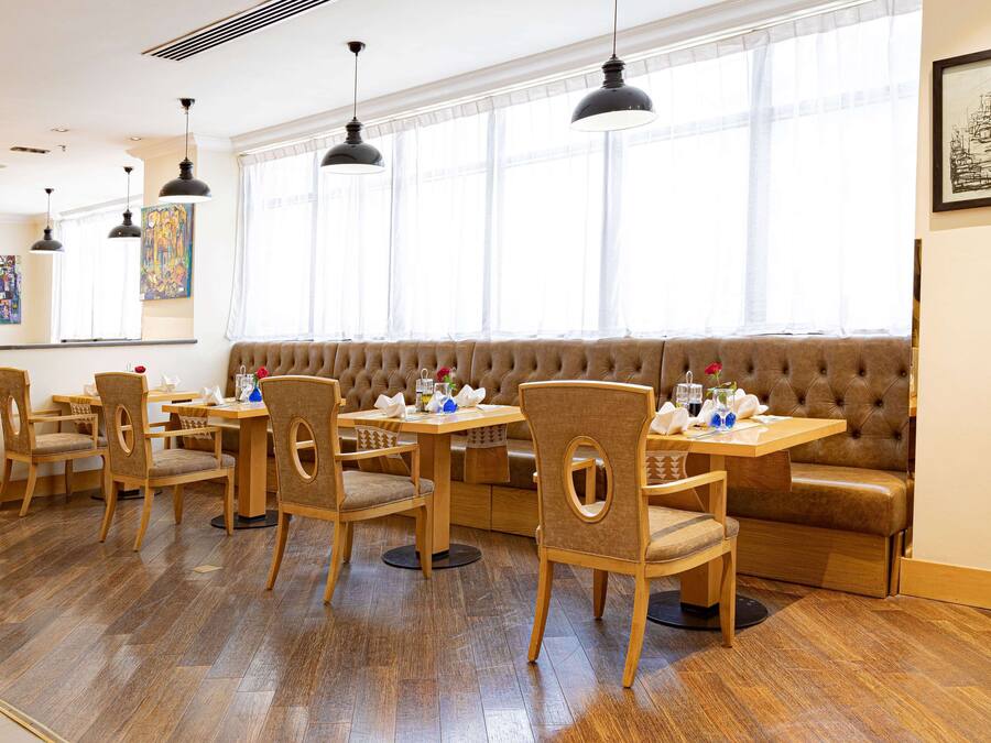 A dining area with wooden tables and chairs, a cushioned bench, and pendant lighting.