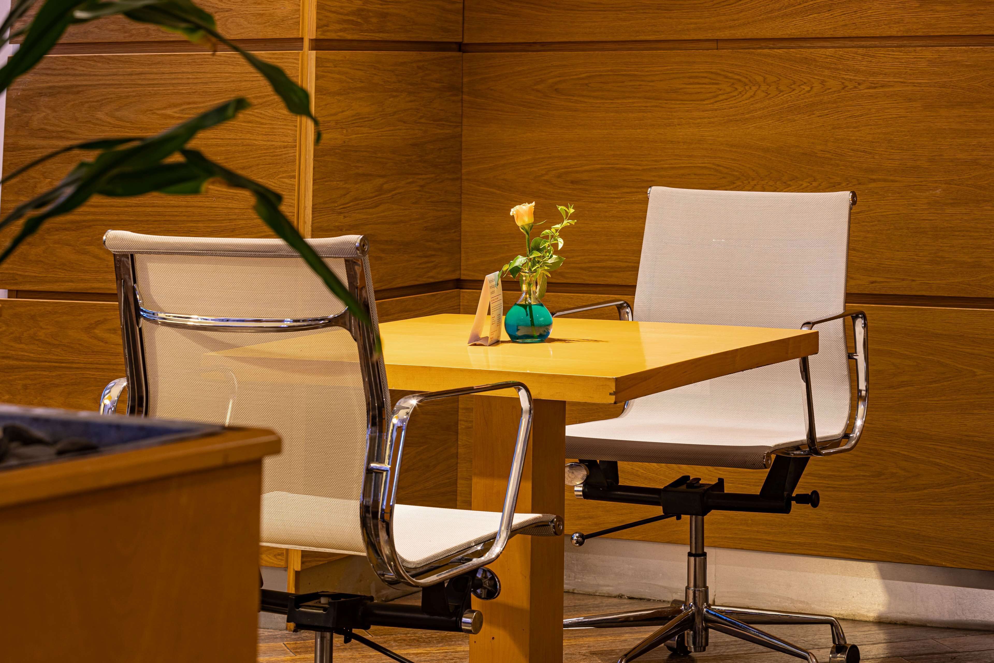 A conference table with two office chairs, a vase with a single flower, and a wooden panel wall.