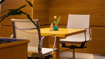 Una mesa de conferencias con dos sillas de oficina, un florero con una sola flor y un panel de pared de madera.
