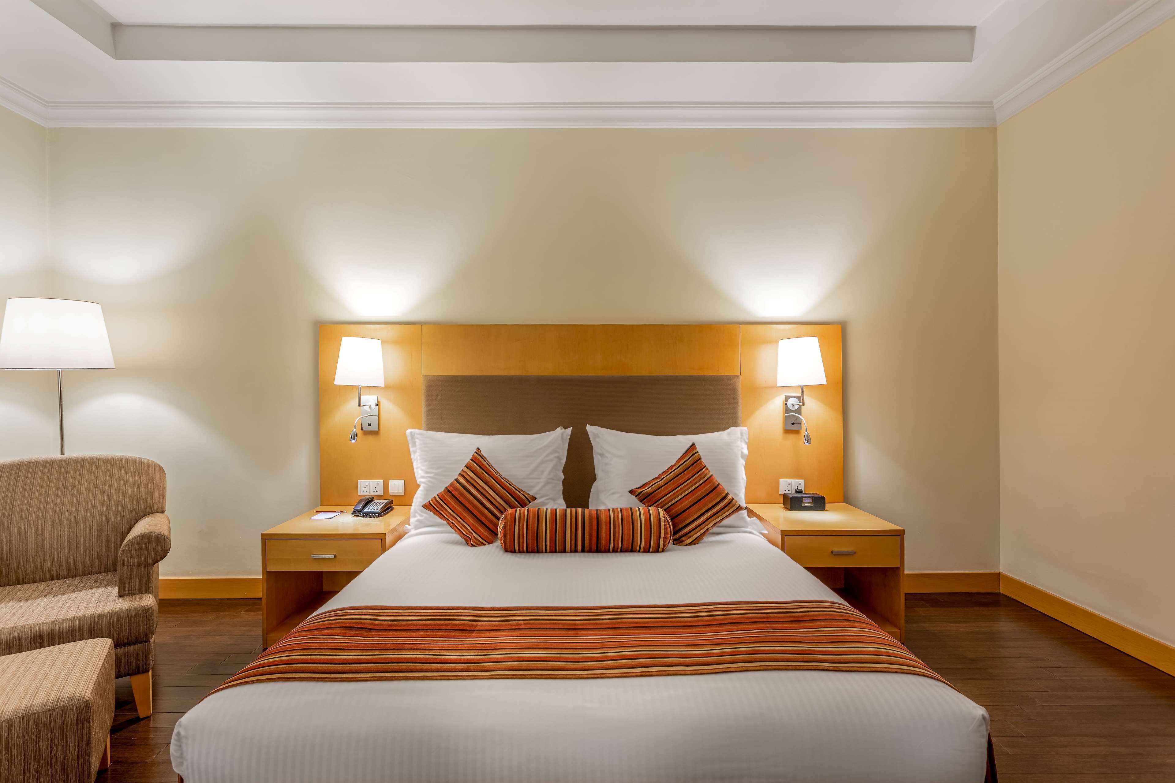 A hotel room with a large bed, two bedside tables, a chair, and a lamp.