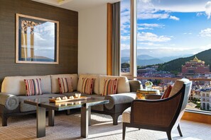 A modern living room with a sofa, armchairs, and a coffee table. A large window offers a view of a cityscape and mountains. - Shangri-La Resort, Shangri-La (Deqin)