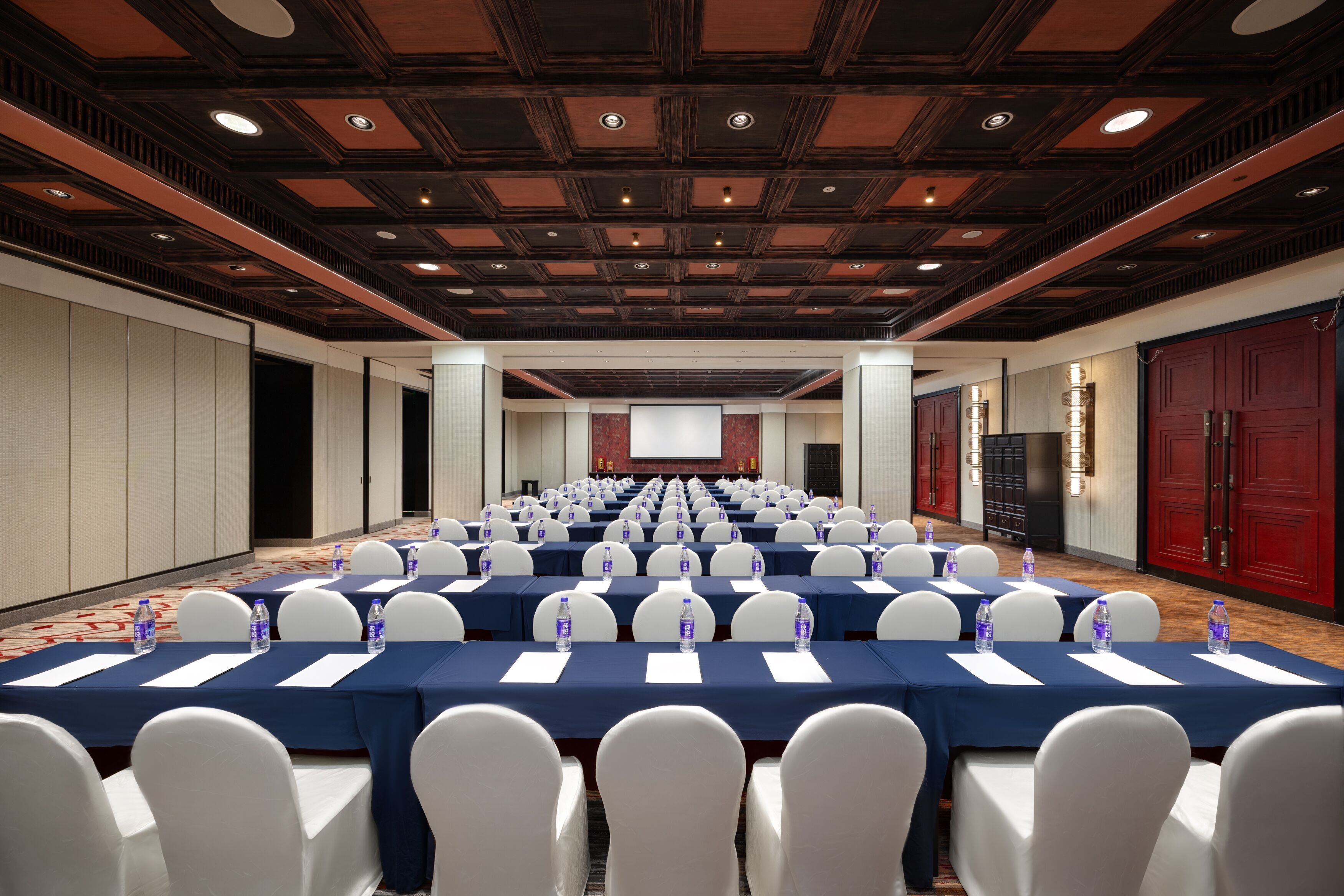 A conference room with rows of tables and chairs, equipped with water bottles and name cards.