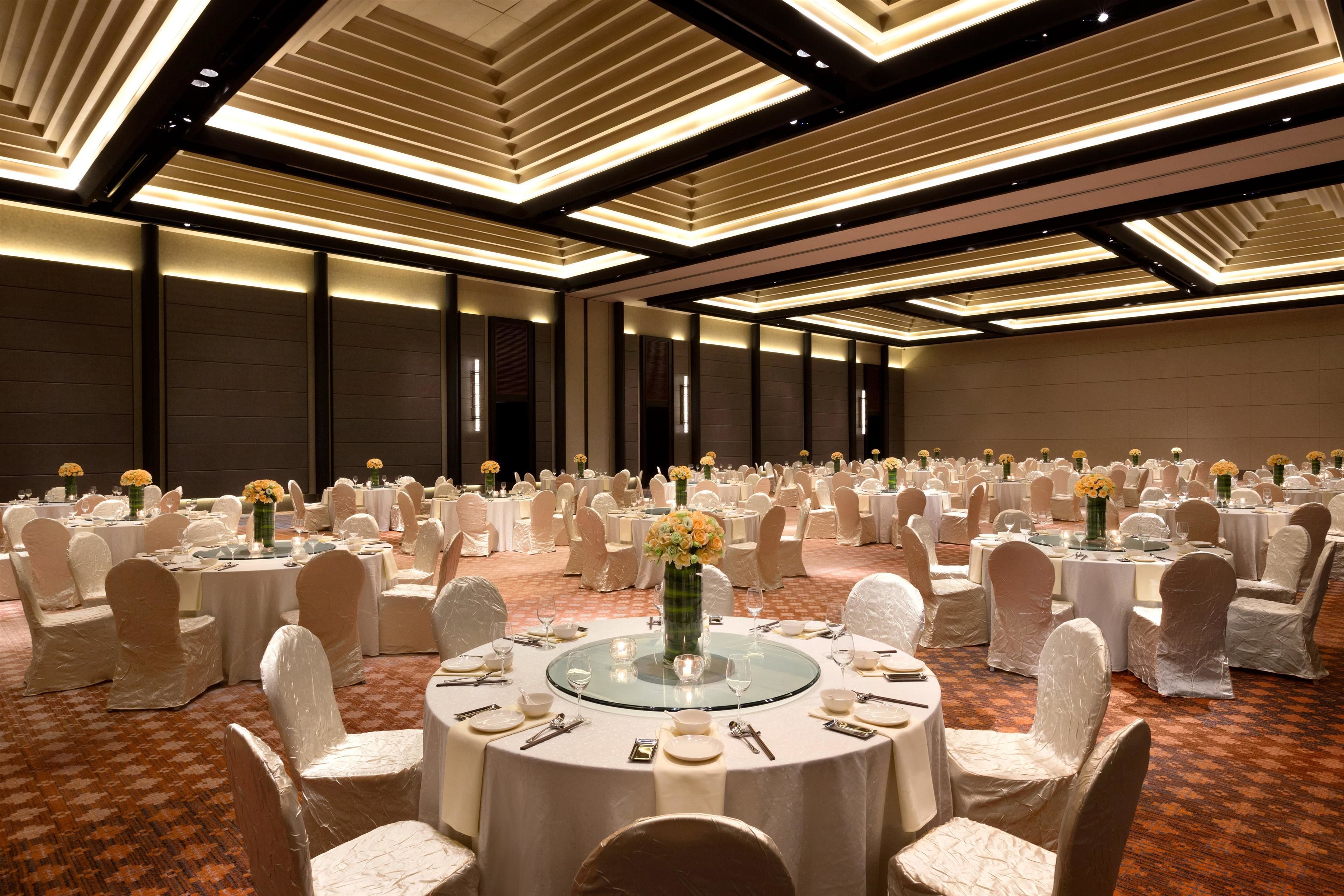 A banquet hall with round tables, white chairs, and floral centerpieces.