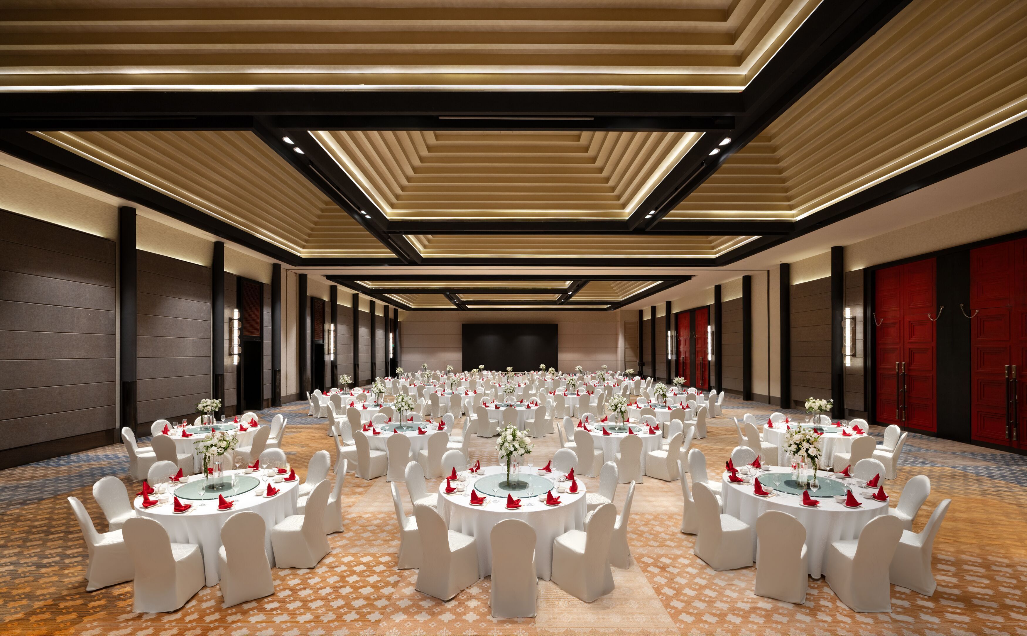 Un amplio salón de banquetes bien iluminado con mesas redondas y sillas blancas, dispuestas en filas.