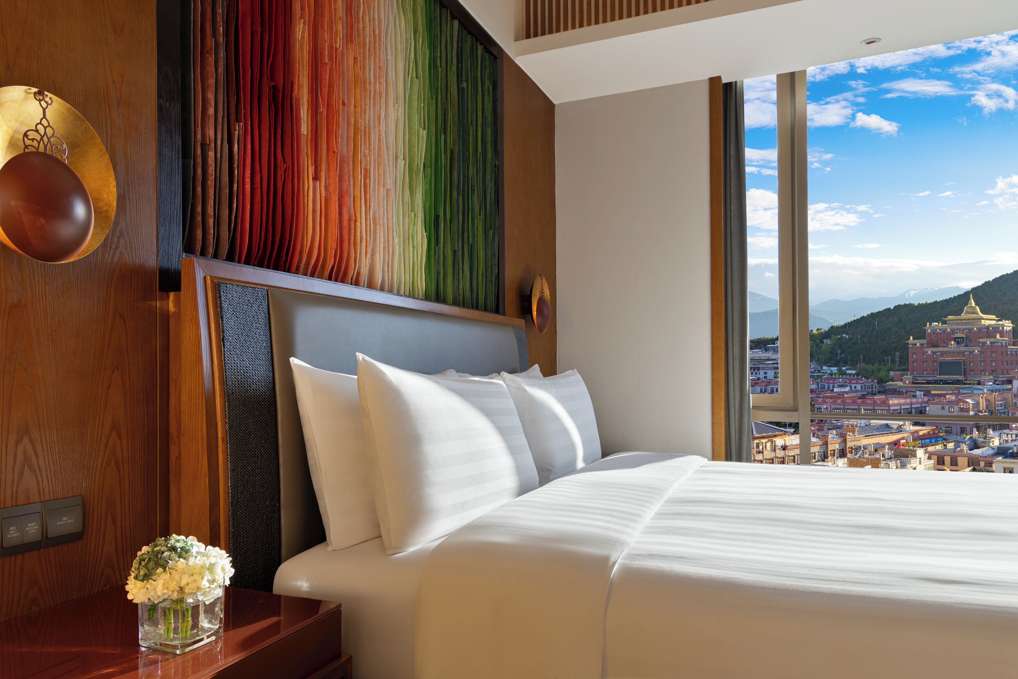 A hotel room with a large bed, a view of a cityscape, and a decorative wall panel.