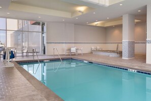 An indoor swimming pool with clear water, a diving board, and a tiled area with chairs. - Embassy Suites by Hilton Kansas City Olathe (Olathe)