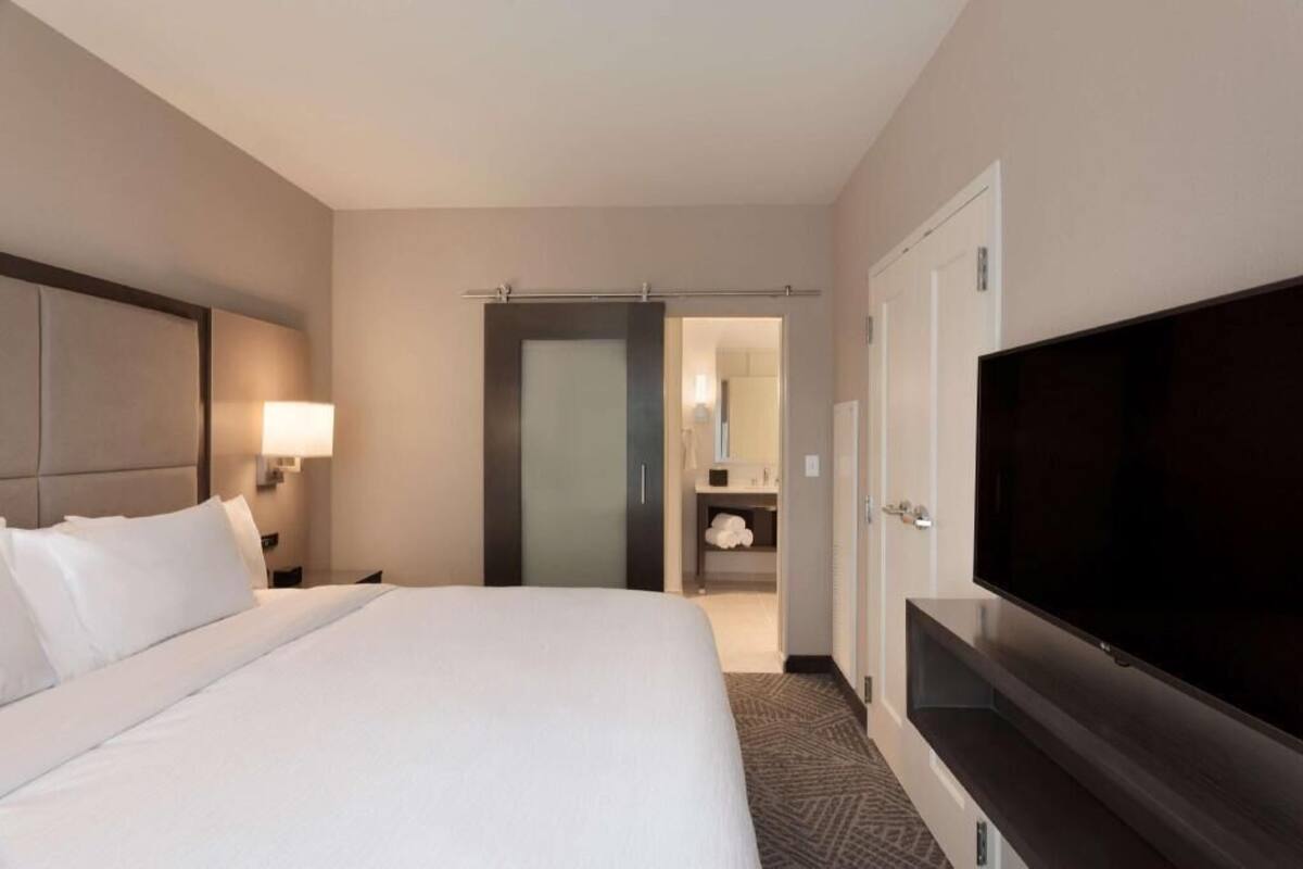 Une chambre d’hôtel comprenant un lit, une télévision, une table de chevet, une lampe, une salle de bain et une porte.