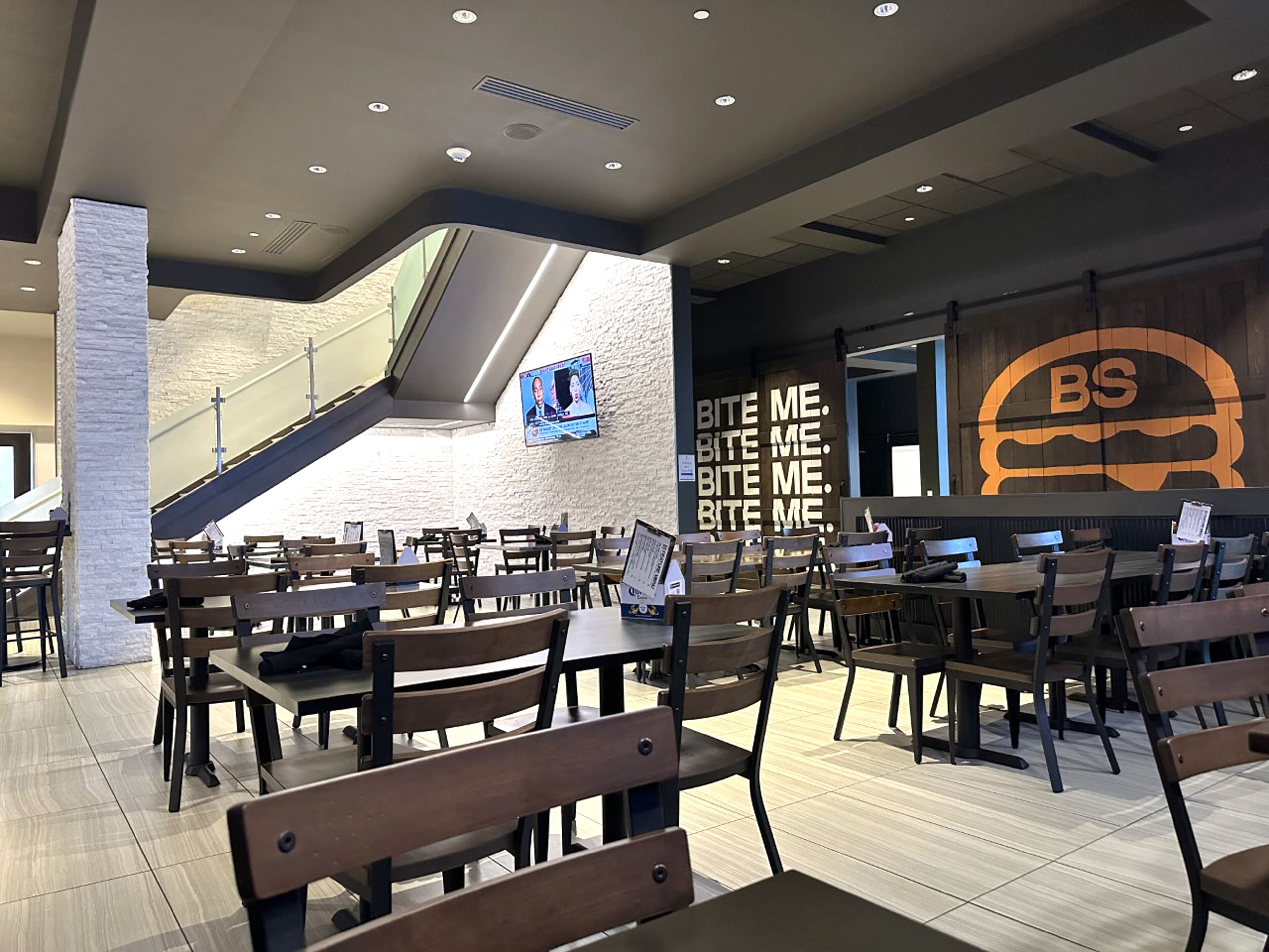 Un restaurante moderno con mesas y sillas de madera, una escalera y una pared con un logotipo grande.