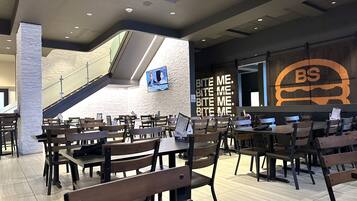 Un restaurante moderno con mesas y sillas de madera, una escalera y una pared con un logotipo grande.