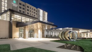 A modern hotel with a prominent entrance, large glass windows, and a unique circular sculpture in the foreground. - Embassy Suites by Hilton Kansas City Olathe (Olathe)