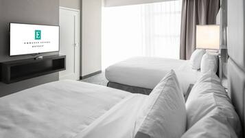 A hotel room with two beds, a TV on a stand, a window with curtains, and a lamp.