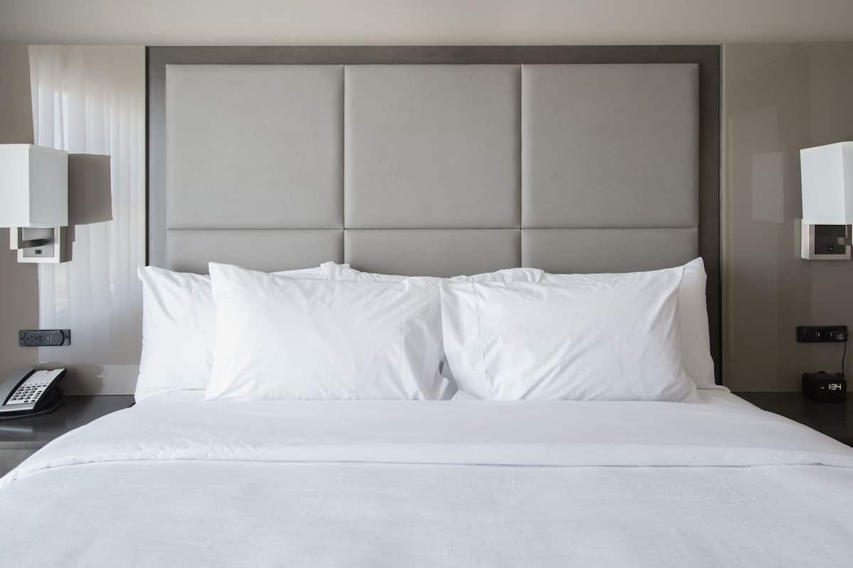 Une chambre d’hôtel avec un grand lit, deux tables de chevet, une commode, un téléphone et deux lampes fixées au mur.