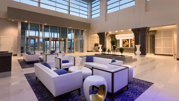A spacious lobby with a high ceiling, large windows, and modern furniture. - Embassy Suites by Hilton Kansas City Olathe (Olathe)