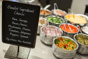 Een bord met een opsomming van ingrediënten voor omeletten, zoals ham, worst, spek, kaas, champignons, uien, tomaten, jalapenos, paprika, spinazie en eiwitten.