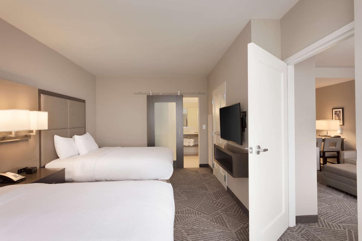 Une chambre d’hôtel avec deux lits, une télévision, un bureau et une salle de bain visible à travers une porte ouverte.