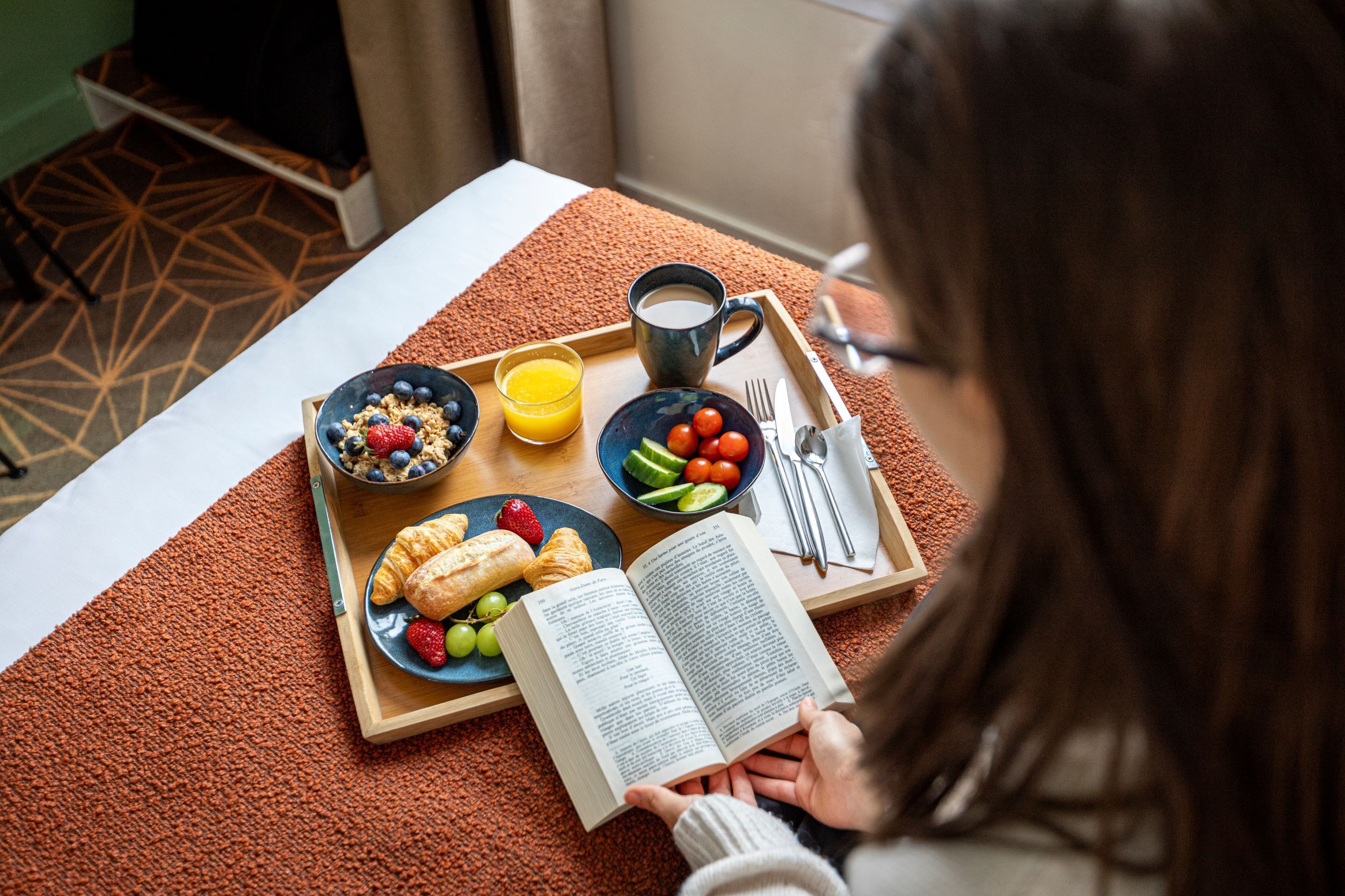 A breakfast tray with croissants, berries, and juice, and a book on a table.