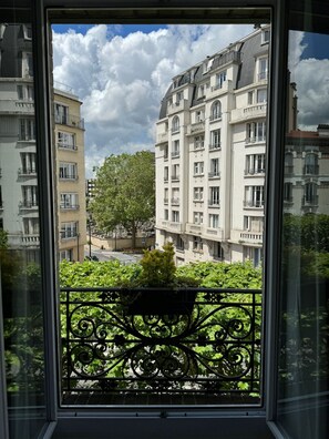 A view from a window of a building with multiple floors, featuring balconies and a large tree in the foreground. - Hotel Olympic Paris Boulogne by Patrick Hayat (Boulogne-Billancourt)