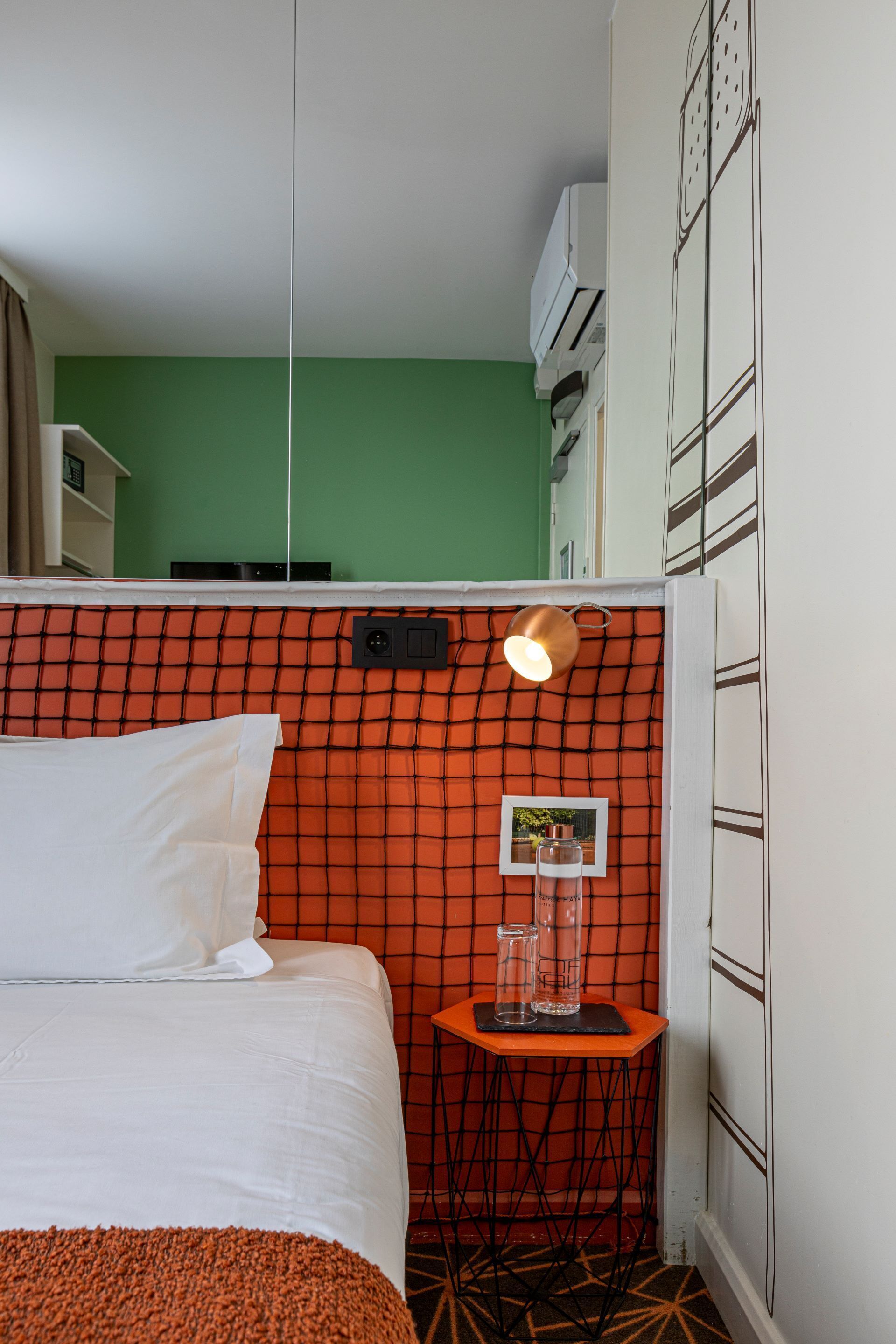 Ein Hotelzimmer mit einem Bett, einem kleinen Tisch mit einer Lampe und einer Wand-Klimaanlage.