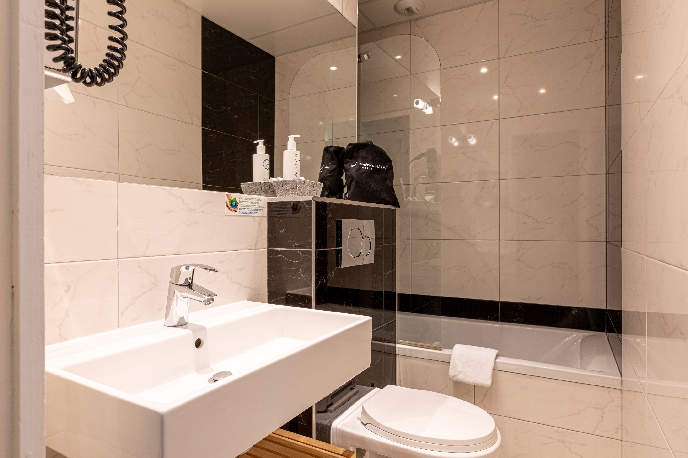 Ein modernes Badezimmer mit einem weißen Waschbecken, einem Spiegel, einer Wand aus schwarzem Marmor, einer Duschkabine aus Glas und einer weißen Toilette.