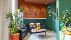 A modern lobby with a green wall, a row of tennis rackets, leather sofas, and potted plants. - Hotel Olympic Paris Boulogne by Patrick Hayat (Boulogne-Billancourt)