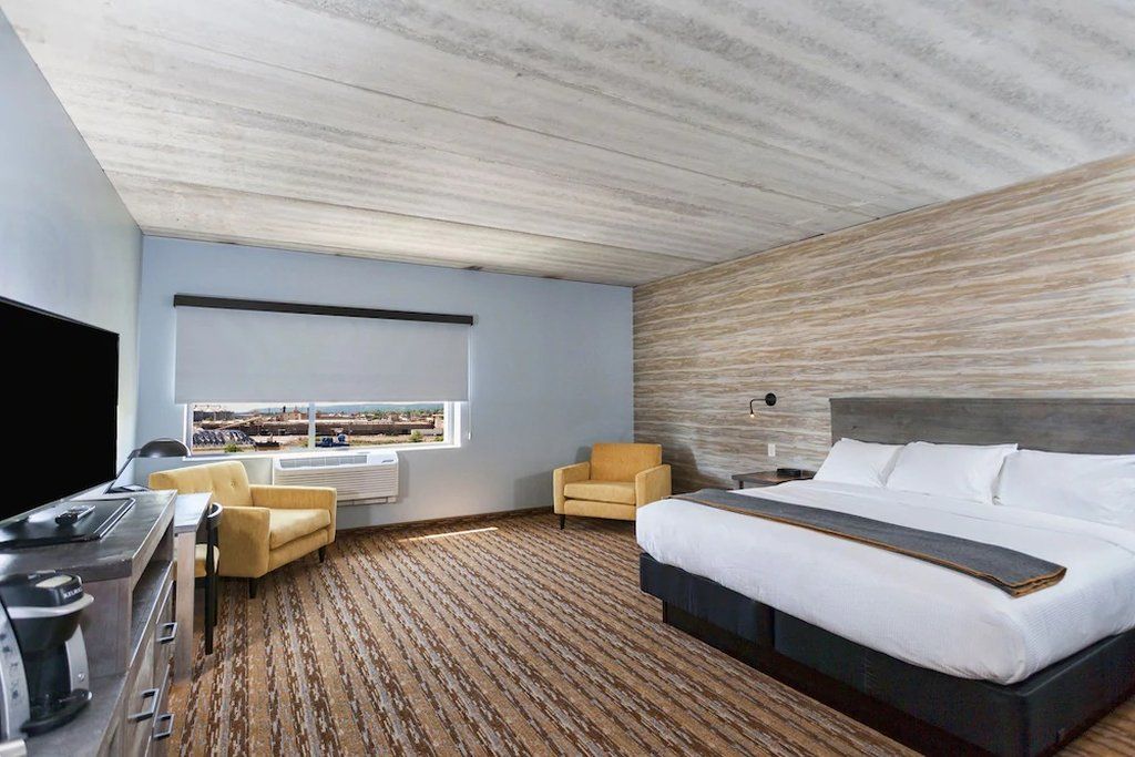 Une chambre d’hôtel moderne dotée d’un grand lit, d’un téléviseur à écran plat, d’un bureau avec une machine à café et offrant une vue sur la ville par la fenêtre.