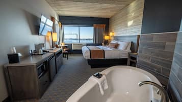 Habitación de hotel con una cama grande, un escritorio con computadora, una lámpara de escritorio, un televisor, una ventana con vista a un puente y una bañera.