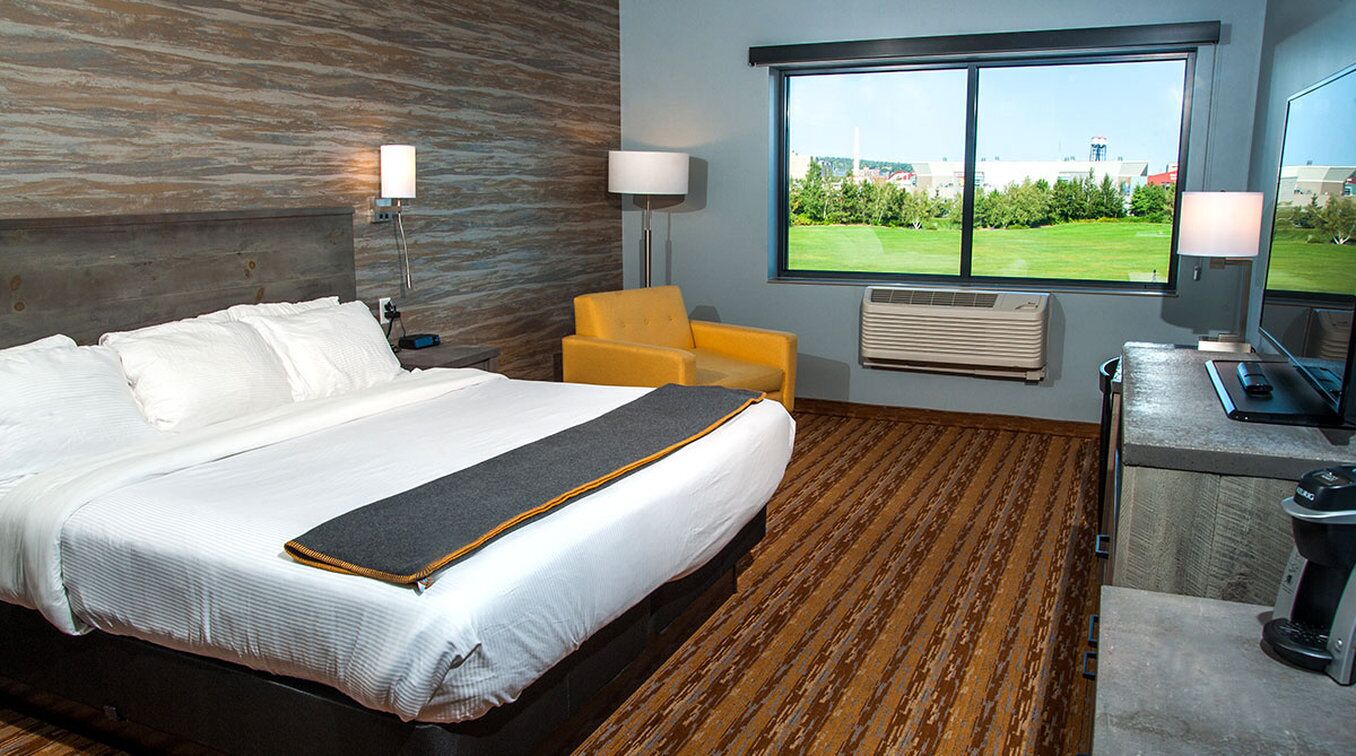 A hotel room with a bed, a chair, a desk, and a large window offering a view.