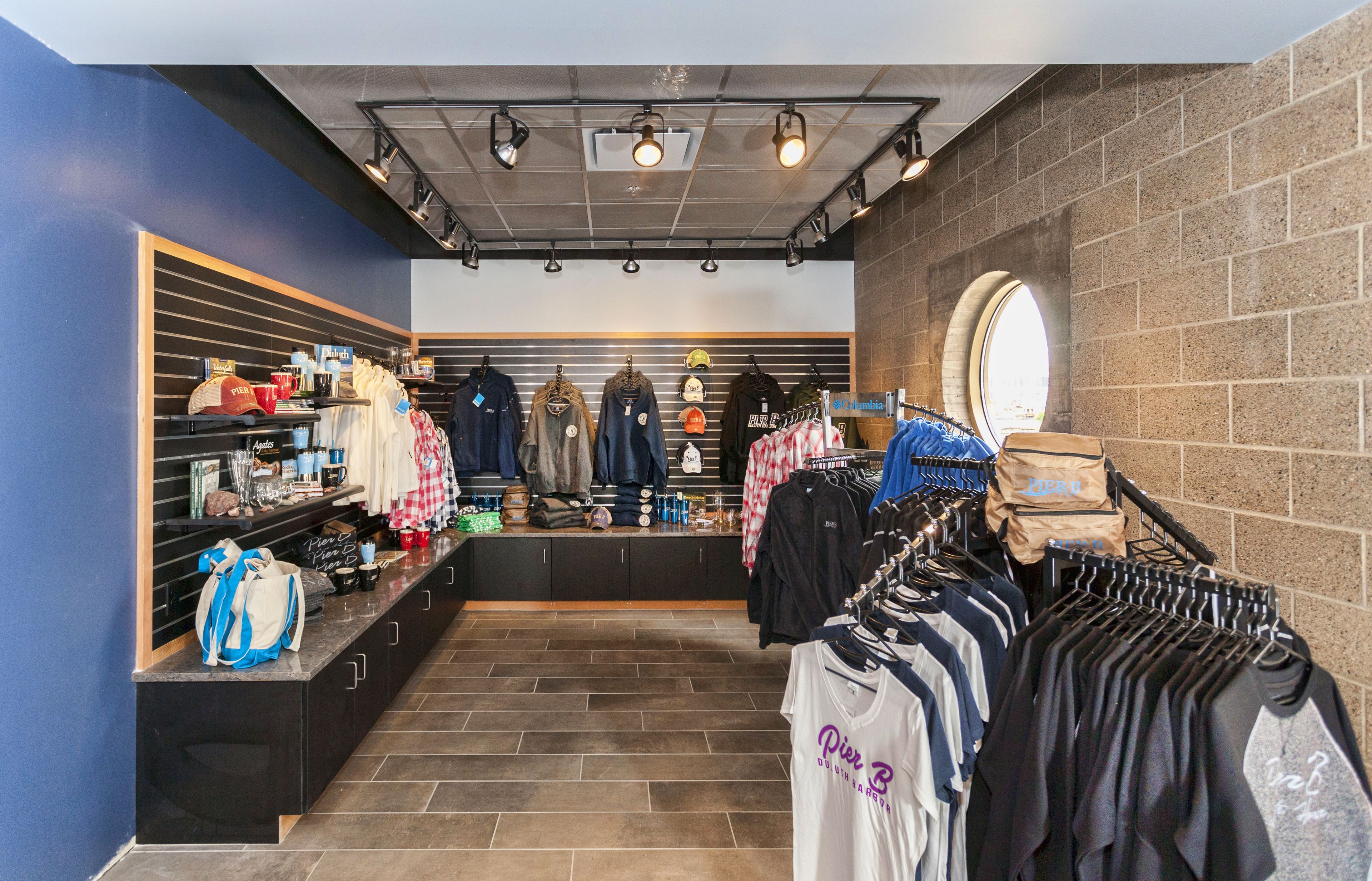 Un magasin de vêtements avec des portants remplis de chemises et de vestes, un comptoir où sont exposés divers articles, et un mur de briques sur l’un des côtés.