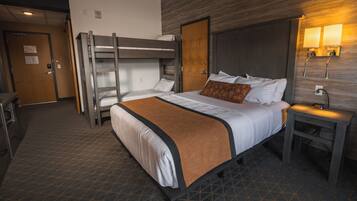 A hotel room with a bunk bed, a single bed, a bedside table with a lamp, and a wall-mounted light fixture.