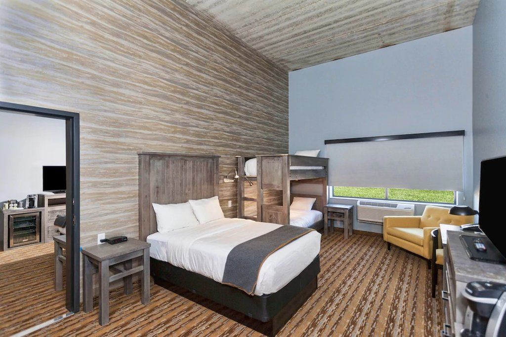 A modern hotel room with a large bed, a desk, a chair, and a view of the outdoors.