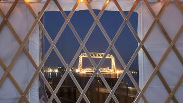 A view through a window with a wooden lattice frame, featuring a cityscape with illuminated structures at night.