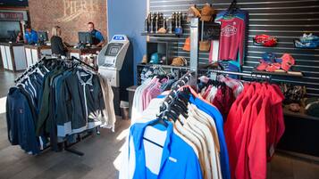 Un magasin de vêtements où l’on trouve des présentoirs remplis de vestes et de chemises, un distributeur automatique de billets et des étagères avec des chapeaux et du matériel de sport.