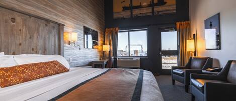 Habitación de hotel con una cama grande, un escritorio, dos sillas, una ventana con vistas a la ciudad y un cuadro de un barco en la pared.