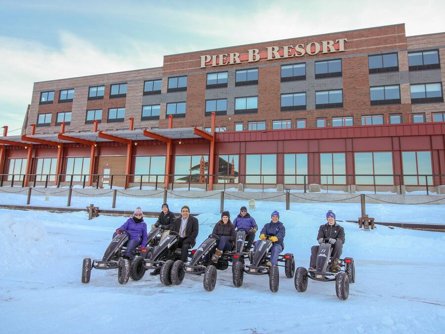 A group of people on snowmobiles in front of a building labeled "Pier B Resort".