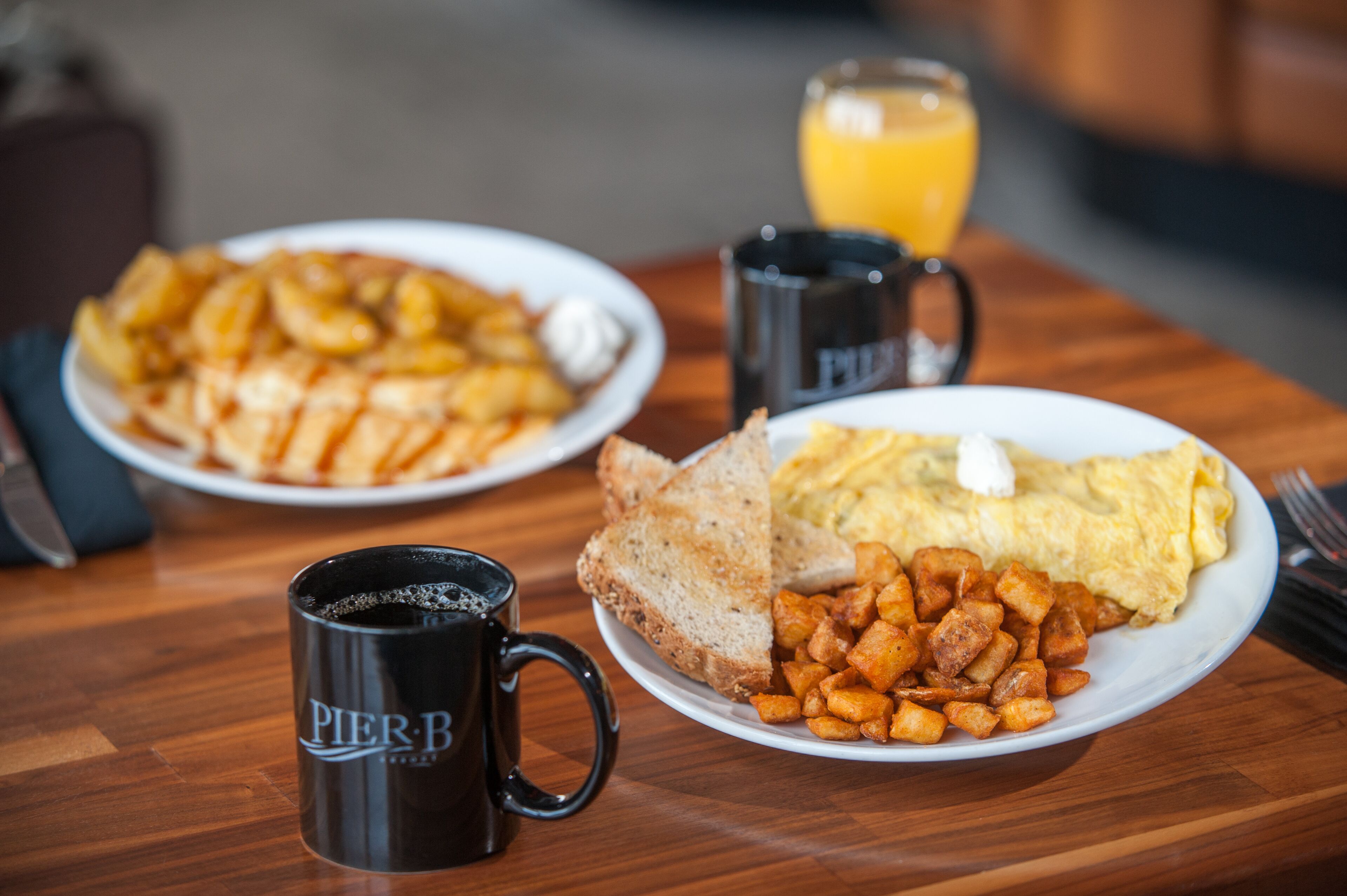A breakfast setting with plates of food, a coffee mug, and a glass of orange juice on a wooden table.