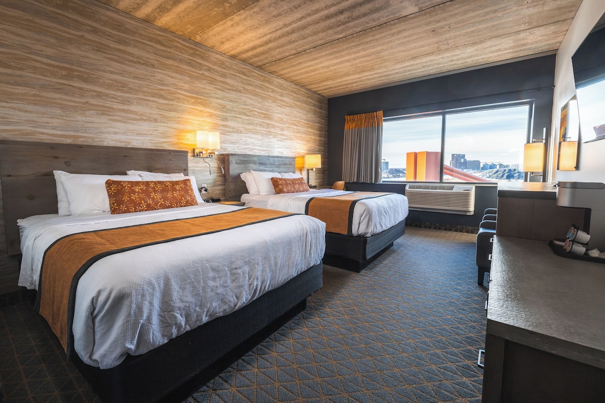 Une chambre d’hôtel avec deux lits, un bureau et une grande fenêtre donnant sur la ville.