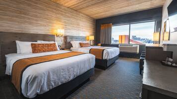 A hotel room with two beds, a desk, and a large window with a city view.