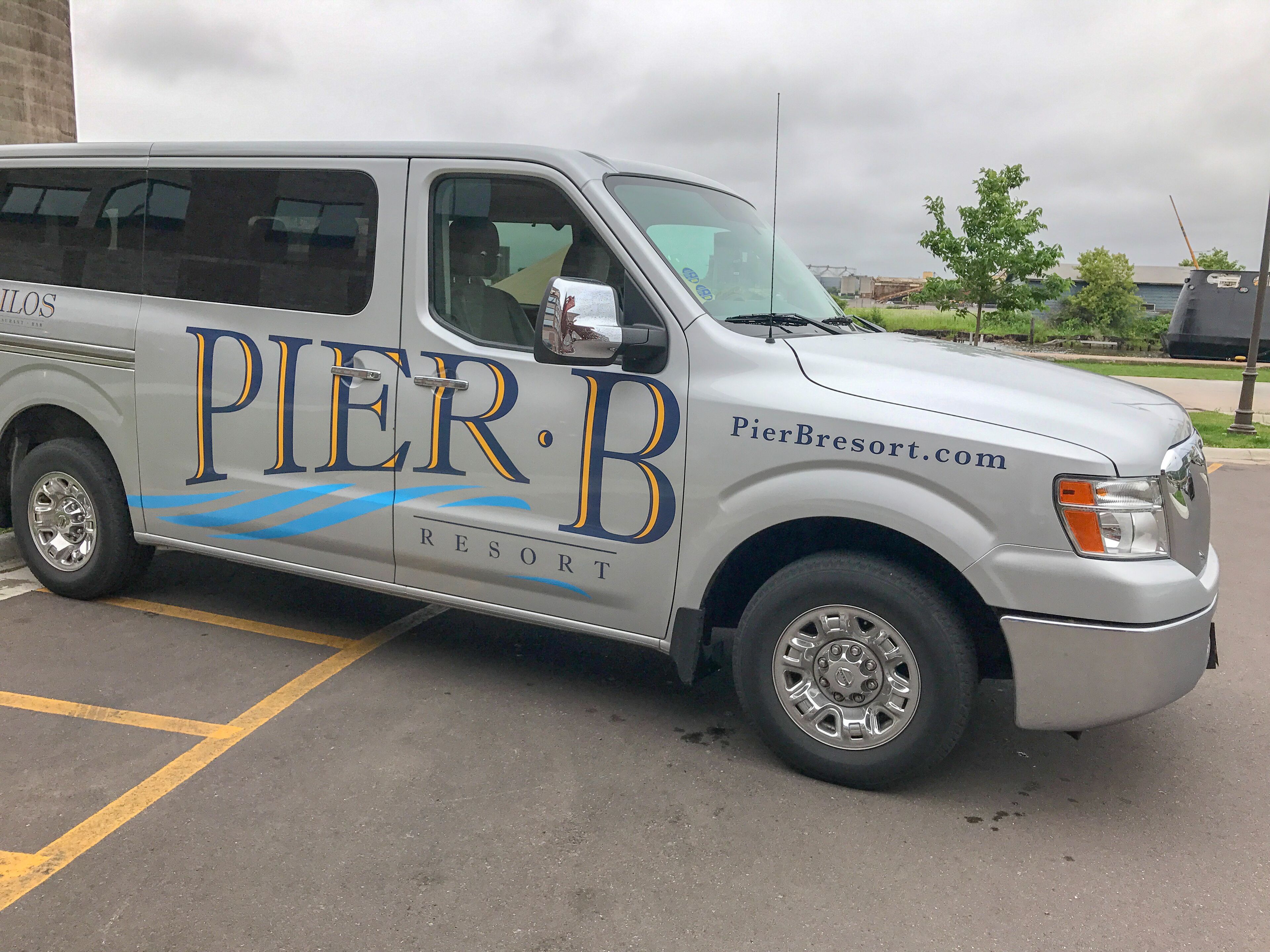 A silver van with 'PierBresort.com' branding, parked in a lot.
