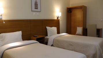 Een hotelkamer met twee bedden, een houten hoofdeinde, nachtlampjes, een lijst met een afbeelding aan de muur, en een houten garderobe.