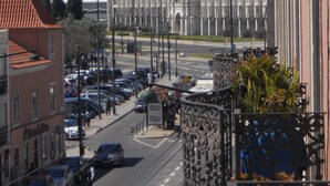 A street view with a large, ornate building in the background, a clear sky, and parked cars along the road. - Belém Tejo - Setubalense (Lisbon)
