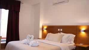 A hotel room with a neatly made bed, a wooden headboard, bedside lamps, and a window with curtains. - Belém Tejo - Setubalense (Lisbon)