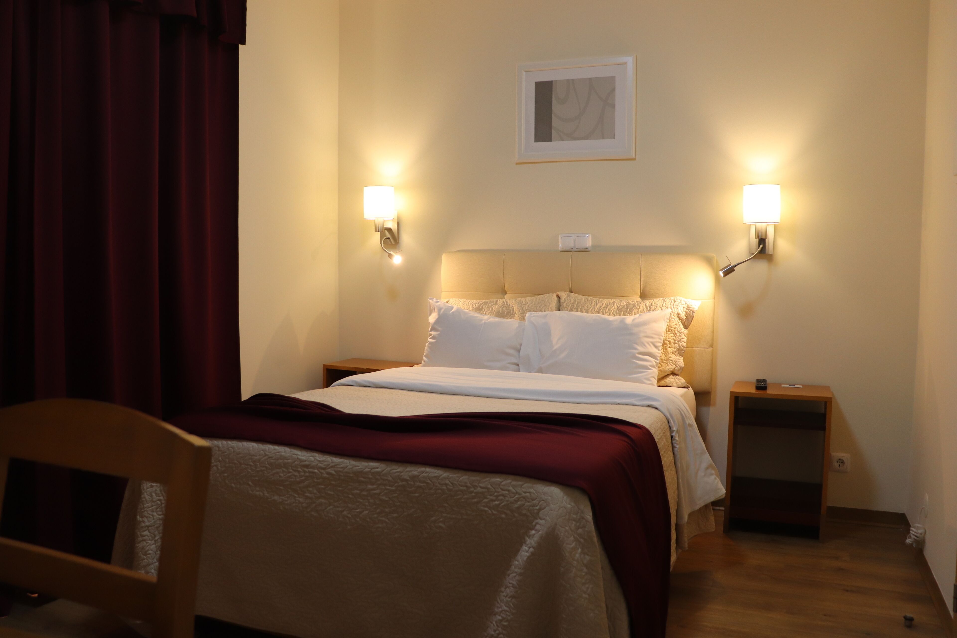 Una habitación de hotel con una cama, dos lámparas de noche, una mesita de noche y una silla.