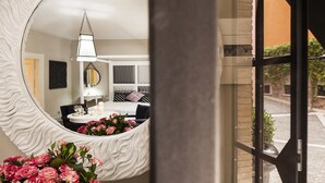 A room with a large mirror, a bed with a white headboard, a bedside table with a lamp, and a view of the outside through a glass door. - Pepoli9 Design Suites in Rome (Rome)