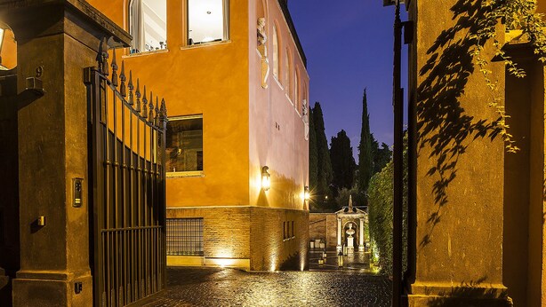 A cobblestone street leading to a building with a gated entrance, a brick wall, and a statue. - Pepoli9 Design Suites in Rome (Rome)