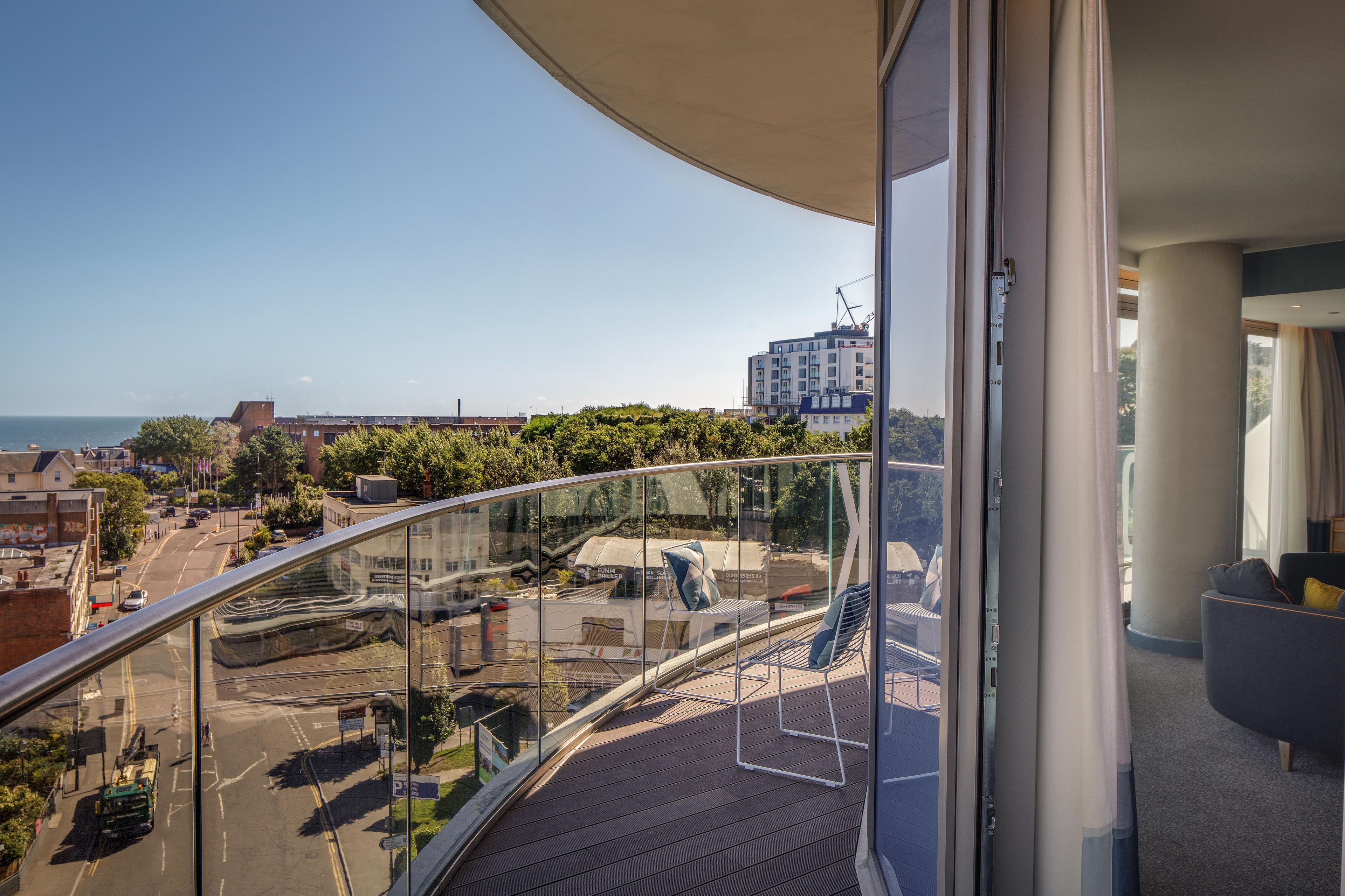 A balcony with a curved glass railing overlooking a cityscape and a body of water.